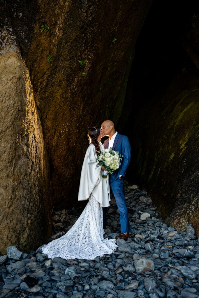 Couple standing on coastal rocks at Arch Cape, Oregon, gazing out over the Pacific Ocean during their elopement.